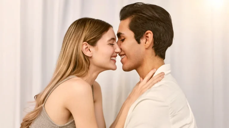 A happy young couple sharing a sweet kiss and smiling, enjoying a joyful moment together outdoors.